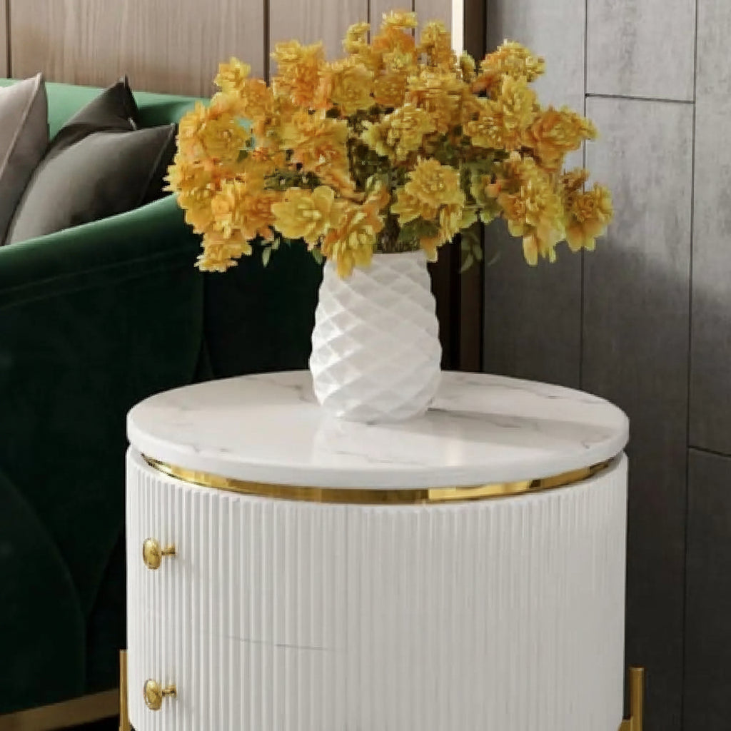 White marble side table with gold accents featuring a vase of yellow flowers in a modern living room setting.

